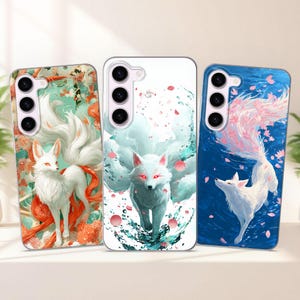 Pode incluir: Três capas de telemóvel com desenhos de raposas. As capas apresentam raposas brancas com várias caudas, contra fundos turquesa, branco e azul. As raposas têm olhos vermelhos e são rodeadas por elementos florais e aquáticos.