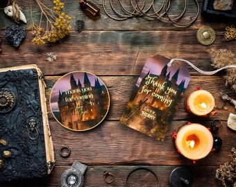 Può includere: Un'etichetta rotonda dorata di ringraziamento con un'immagine di un castello di notte. Il testo sull'etichetta dice "Grazie per essere venuto! Con affetto, Hermy".