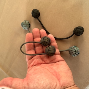 May include: Five handmade knotted balls with strings attached. The balls are green, black, and brown. The strings are black.