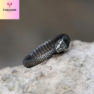 Puede incluir: Un anillo de serpiente de plata con un diseño detallado de cabeza de serpiente. El anillo está hecho de acero inoxidable y tiene un acabado texturizado.