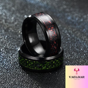Könnte beinhalten: Zwei schwarze Ringe mit komplizierten keltischen Knotenmustern. Ein Ring hat eine rote Einlage, der andere eine grüne Einlage.