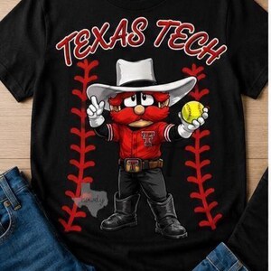 Könnte beinhalten: Ein schwarzes kurzärmeliges T-Shirt mit dem roten Schriftzug TEXAS TECH. Die Grafik zeigt eine Zeichentrickfigur mit weißem Cowboyhut, rotem Hemd mit Logo, schwarzer Hose und Stiefeln, die einen gelben Softball zwischen zwei roten Baseballnähten hält.