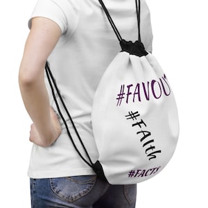 May include: White drawstring backpack with black drawstrings and a black closure. The bag features the words "#FAVOU", "#Faith", and "#FACTS" in purple and black lettering. The bag is worn over the shoulder.