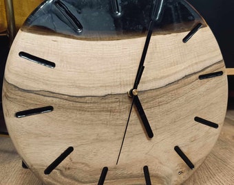 Puede incluir: Un reloj redondo de madera con detalles de resina epoxi negra. La esfera del reloj tiene marcadores de hora negros y agujas negras.