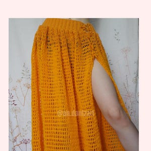 May include: A handmade, bright orange crochet skirt with a high slit. The skirt is made of a loosely woven, open stitch pattern. The skirt is a vibrant, solid color and appears to be a maxi length.