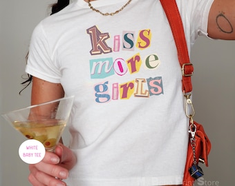 Könnte beinhalten: Ein weißes, kurzärmeliges Baby-T-Shirt mit einem Grafikdruck, der den Text "kiss more girls" in einer farbenfrohen Collage-Schrift zeigt. Die Buchstaben sind in verschiedenen Farbtönen gehalten, darunter Violett, Pink, Blau, Gelb und Grün, mit einer Textur.