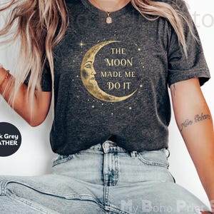 May include: A dark grey heather t-shirt with a gold crescent moon graphic and the text "The Moon Made Me Do It".