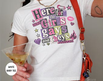 Könnte beinhalten: Weißes Baby-T-Shirt mit dem Text "Here for the Girls gays and theys" in einem farbenfrohen Collage-Stil. Das Shirt hat rosa, lila und grüne Buchstaben mit dekorativen Elementen wie Sternen, Herzen und einem Kussmund.
