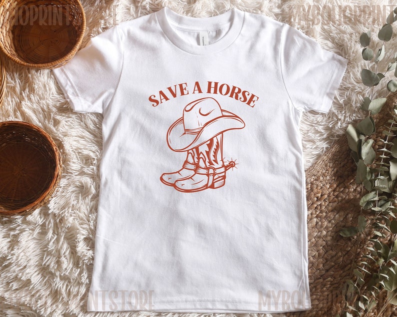 May include: White t-shirt with a red graphic of a cowboy hat and boots. The text "Save a Horse" is above the graphic.