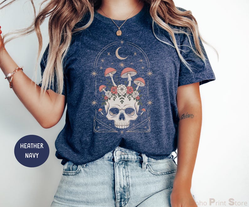 May include: Heather navy blue t-shirt featuring a skull design with mushrooms, flowers, and a crescent moon. The graphic is in a vintage style with a celestial theme. The shirt is made of a soft material.