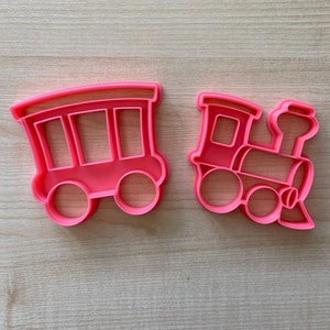 Può includere: Due tagliabiscotti in plastica rosa a forma di locomotiva e vagone.