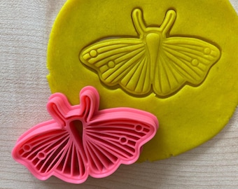 May include: A pink plastic butterfly cookie cutter with a yellow butterfly imprint in a piece of yellow dough.