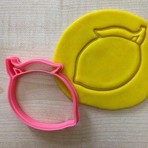Könnte beinhalten: Ein rosa Plastik-Keksstempel in Form einer Zitrone mit einem gelben Fondant-Abdruck einer Zitrone.