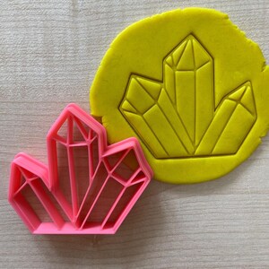 May include: Pink and yellow plastic cookie cutters shaped like geometric crystals.