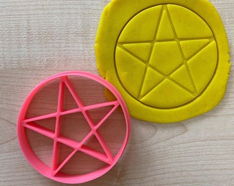 Puede incluir: Un cortador de galletas de plástico rosa en forma de estrella de cinco puntas con un círculo de masa amarilla detrás.