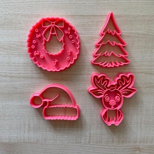 Op de afbeelding: Vier roze plastic kerstkoekjesvormen: een krans met de woorden "Woo 2020", een kerstboom, een kerstmanmuts en een rendier.