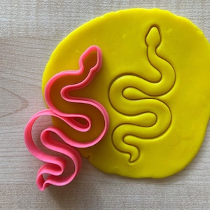 Op de afbeelding: Een roze plastic slangkoekjesvormer met een gele fondant slangenafdruk.