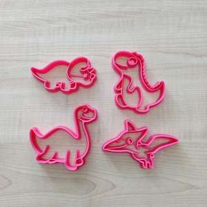 Peut inclure: Quatre emporte-pièces en plastique rose en forme de dinosaures. Les emporte-pièces sont en forme de tricératops, de stégosaure, de ptérodactyle et de tyrannosaure rex.