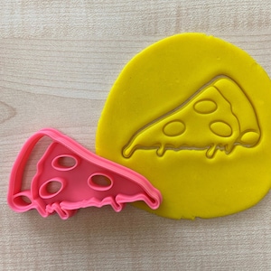Może przedstawiać: Różowa plastikowa foremka do ciasteczek w kształcie kawałka pizzy z odciskiem kawałka pizzy z żółtej masy cukrowej.