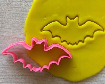 Könnte beinhalten: Ein rosa Plastik-Fledermaus-Ausstecher auf einer gelben Oberfläche mit einem Abdruck einer Fledermaus, der vom Ausstecher gemacht wurde.