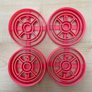 Può includere: Quattro formine rosa per biscotti a forma di dischi per pesi. Ogni formina mostra un numero diverso: 2, 10, 5 e 25. Le lettere "kg" sono stampate su ciascuna, indicando i chilogrammi.