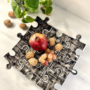 Può includere: Vassoio da portata in ceramica bianco e nero a forma di puzzle, con un melograno, uva e noci in cima.