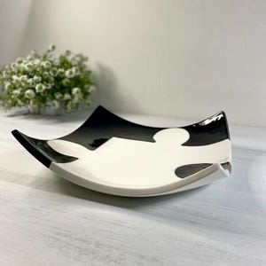 Könnte beinhalten: Ein quadratischer, dekorativer Keramikteller mit einem schwarz-weißen Puzzleteil-Design. Der Teller hat eine glänzende Oberfläche und gebogene Kanten. Der schwarze Bereich befindet sich oben und der weiße Bereich unten.