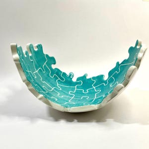 Peut inclure: Un bol en céramique blanche avec un glaçage bleu turquoise. Le bol est en forme de pièce de puzzle et a un design moderne et unique.