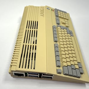 以下が含まれることがあります： ベージュの Amiga コンピューターで、グレーのキーボードと上部に「AMIGA」という文字が印刷されています。コンピューターには前面に一連のスロットがあります。