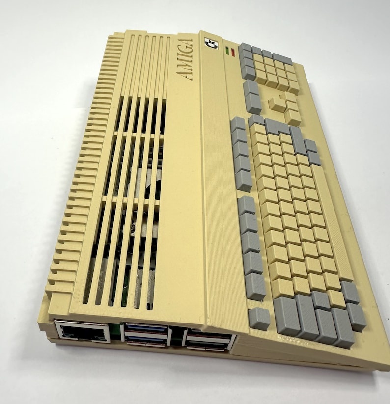 以下が含まれることがあります： ベージュの Amiga コンピューターで、グレーのキーボードと上部に「AMIGA」という文字が印刷されています。コンピューターには前面に一連のスロットがあります。
