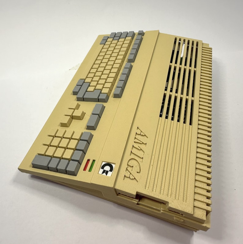 以下が含まれることがあります： ベージュのAmigaコンピュータで、キーボードと換気口があります。コンピュータには黒と緑のロゴがあり、側面に「AMIGA」と印刷されています。