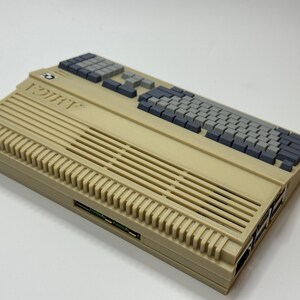 以下が含まれることがあります： グレーのキーボードと側面に複数のスロットが付いたベージュ色のアタリ 800 XL コンピューターです。