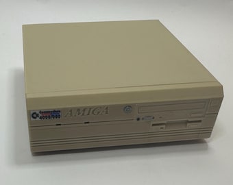 以下が含まれることがあります： ベージュ色のCommodore Amiga 4000/060コンピュータ。コンピュータの前面には、フロッピーディスクドライブスロット、CD-ROMドライブスロット、電源ボタンがあります。Amigaのロゴが見えます。