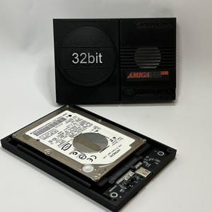 May include: A black Amiga CD32 console with a 32-bit label and a hard drive with a Hitachi logo.