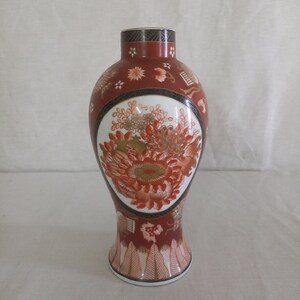 Può includere: Un vaso in ceramica rosso e bianco con un motivo floreale. Il vaso ha un corpo rotondo e un collo stretto. Il motivo floreale è in tonalità di rosso, arancione e oro.