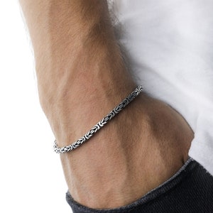 This bracelet, which is made of 925 sterling silver, has a thick chain. There are intertwined shapes in this chain. These shapes form a pattern in the overall appearance.