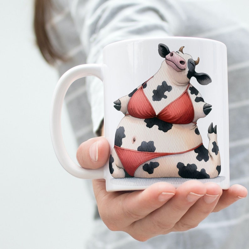 May include: White ceramic mug with a black and white cow wearing a red bikini. The cow is sitting on a white background.