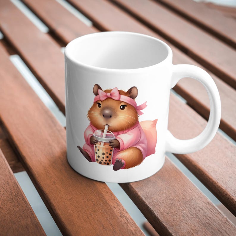 May include: White ceramic mug with a cartoon illustration of a brown hamster wearing a pink headband and pink sweater, drinking a bubble tea with a straw.