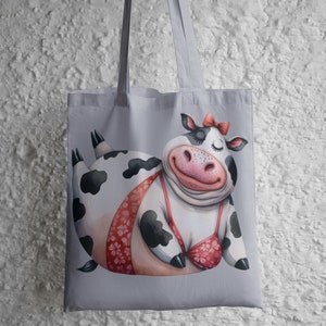 May include: A gray tote bag with a cartoon illustration of a black and white cow wearing a pink bikini. The cow is smiling and has its eyes closed.