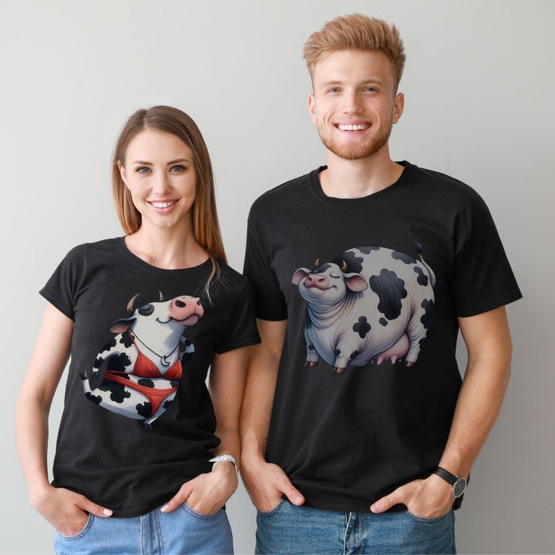 May include: Two black t-shirts with a cow graphic. One shirt features a cow wearing a bikini and the other shirt features a cow with a relaxed expression.