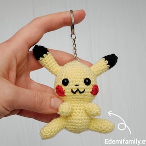 May include: A yellow crocheted Pikachu keychain with black ears and red cheeks. The keychain is attached to a silver chain.