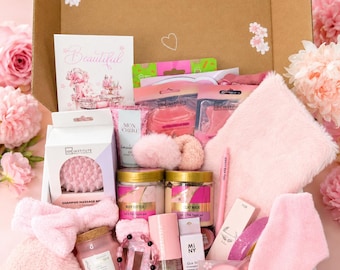 May include: A gift box filled with pink beauty products including a shampoo massage brush, body butter, clay mask, a fuzzy headband, a pink pen with the text YOU ARE LOVED, a candle, a gua sha tool, lip pads, and a small beaded bracelet.