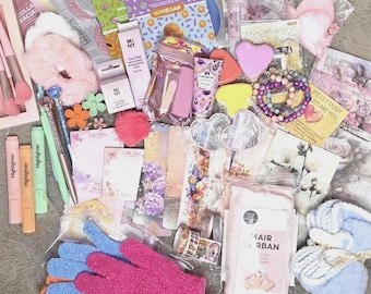 Pode incluir: Uma coleção de artigos de beleza e papelaria, incluindo elásticos de cabelo rosa, marcadores de texto, canetas, uma ferramenta gua sha, máscaras faciais, acessórios em forma de coração, pulseiras de contas, marcadores de página florais, fita adesiva decorativa, luvas esfoliantes e um turbante para cabelo.