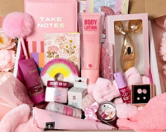 May include: A gift box containing a pink notebook with the text TAKE NOTES, a pink pen with a pom-pom, a tube of body lotion, a gold facial roller, a rainbow-shaped sponge, a jar of cherry scrub, a lip gloss, a candle, and small stud earrings.