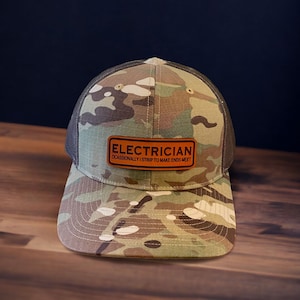May include: A camouflage trucker hat with a brown leather patch that reads "Electrician Occasionally I Strip To Make Ends Meet".