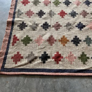 May include: A beige rug with a geometric pattern of colourful diamonds. The rug has a dark blue border.