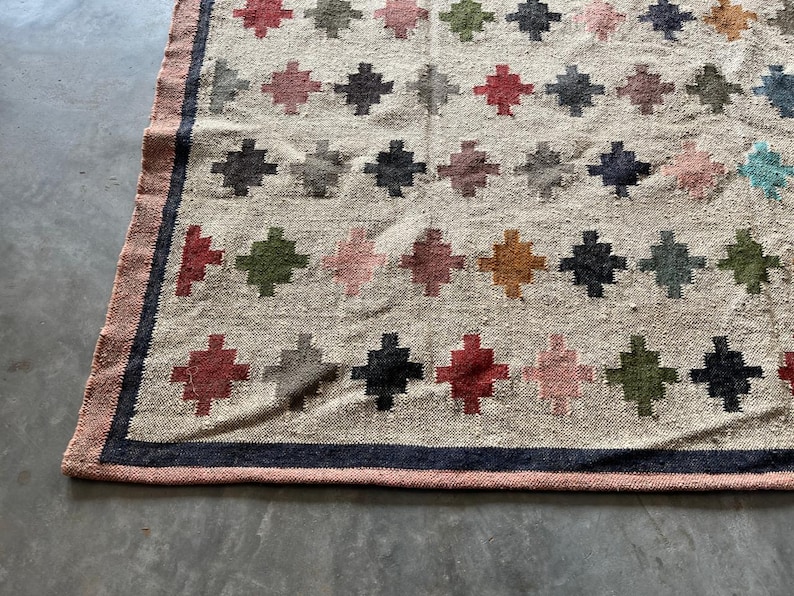 May include: A beige rug with a geometric pattern of colourful diamonds. The rug has a dark blue border.