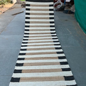Puede incluir: Una alfombra larga y estrecha de rayas blancas y negras hecha de fibras naturales. La alfombra está tejida con rayas blancas y negras alternas, y las rayas tienen aproximadamente 2,5 cm de ancho.