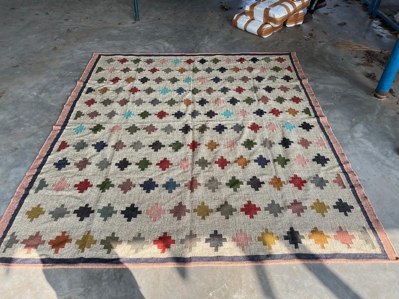 May include: A beige area rug with a geometric pattern of colourful diamonds. The rug has a dark brown border.