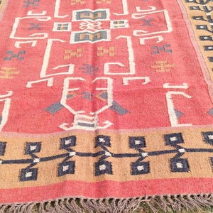 May include: A red, brown, and black patterned rug with a geometric design. The rug has a fringe border.
